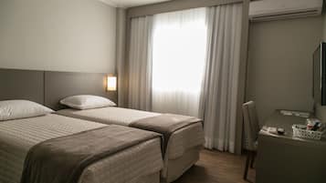 Habitación de hotel con dos camas, un escritorio, una silla y un ventanal grande con cortinas.