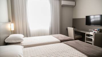 A hotel room with two beds, a desk, a chair, a TV, and an air conditioning unit.
