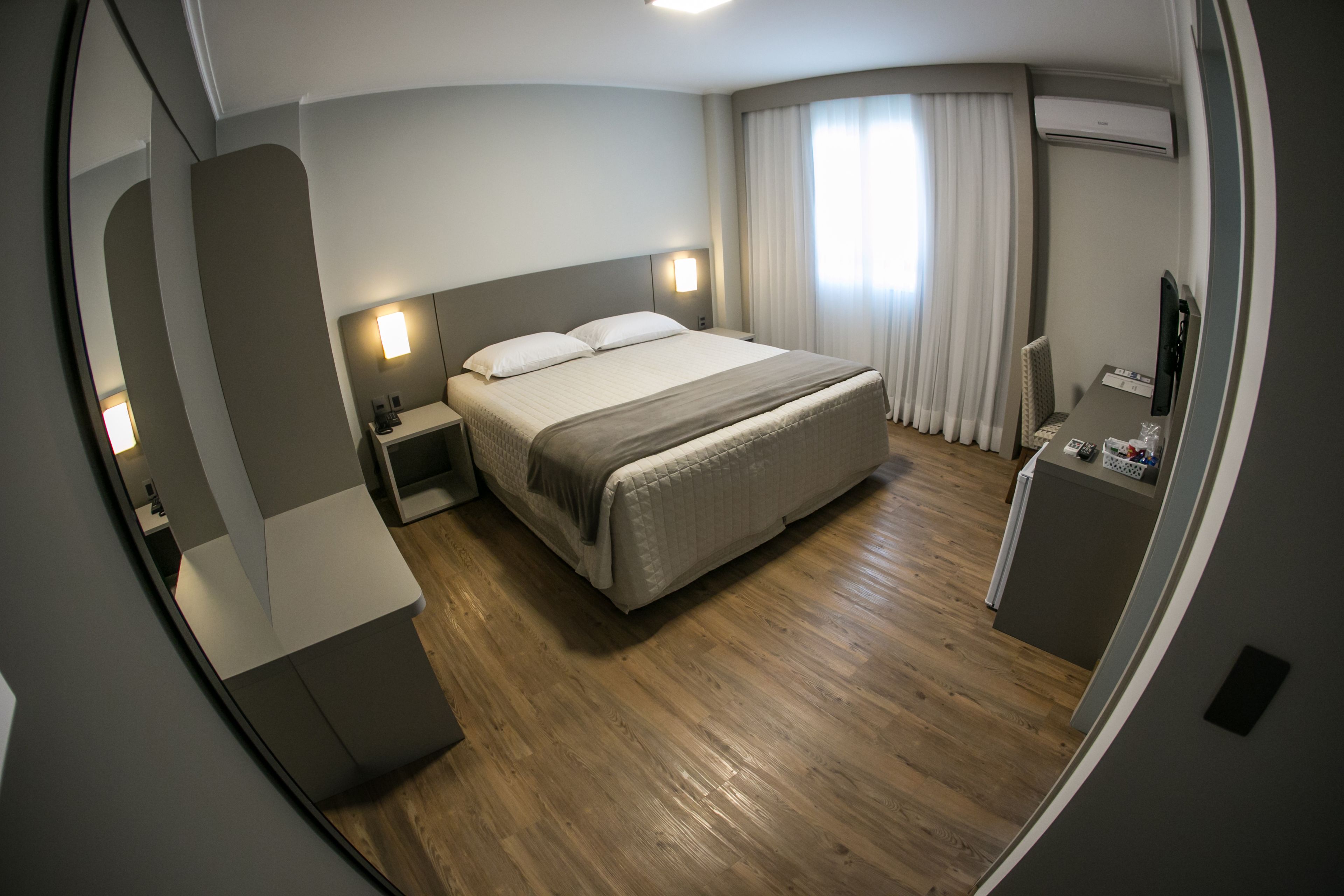 A hotel room with a bed, bedside tables, a desk, and a television.