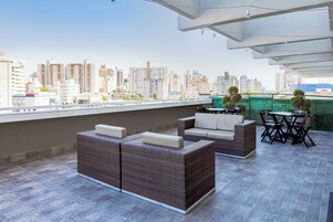 Una terraza en la azotea con mobiliario de mimbre, vistas del horizonte urbano y un seto verde.