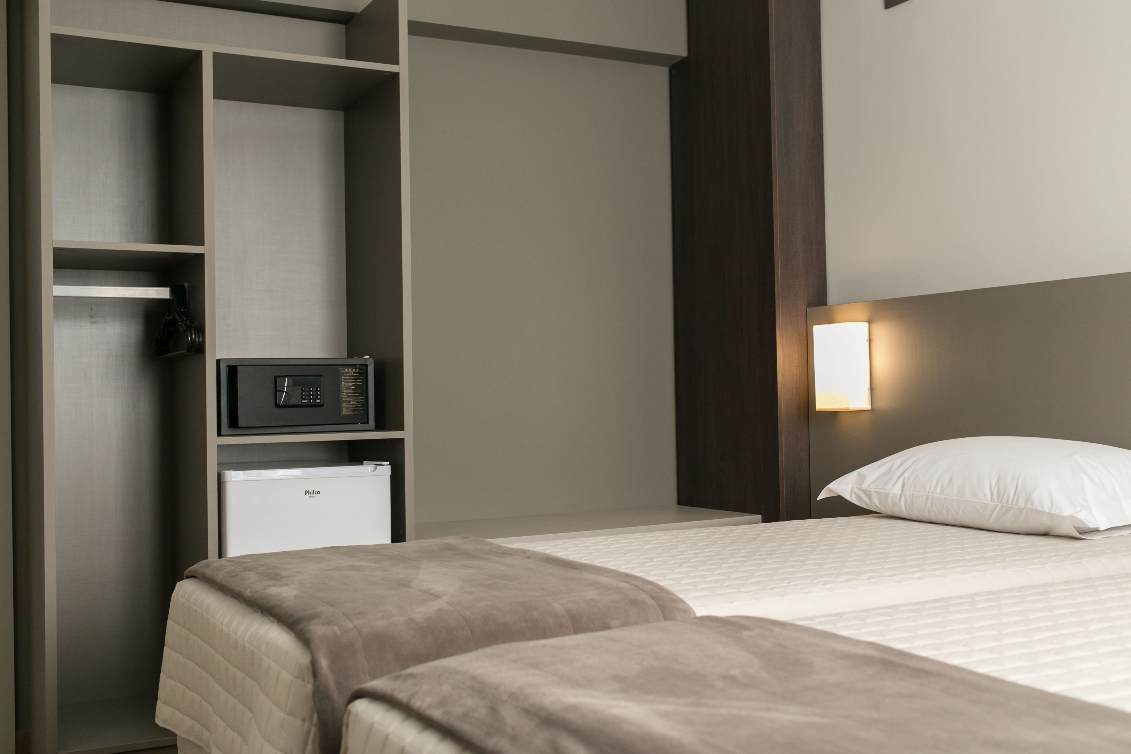 A hotel room with two beds, a minibar, and a wall-mounted light fixture.