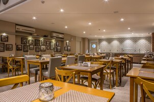 Un comedor con varias mesas y sillas, cuadros en las paredes y un salpicadero de cocina con un diseño decorativo.
