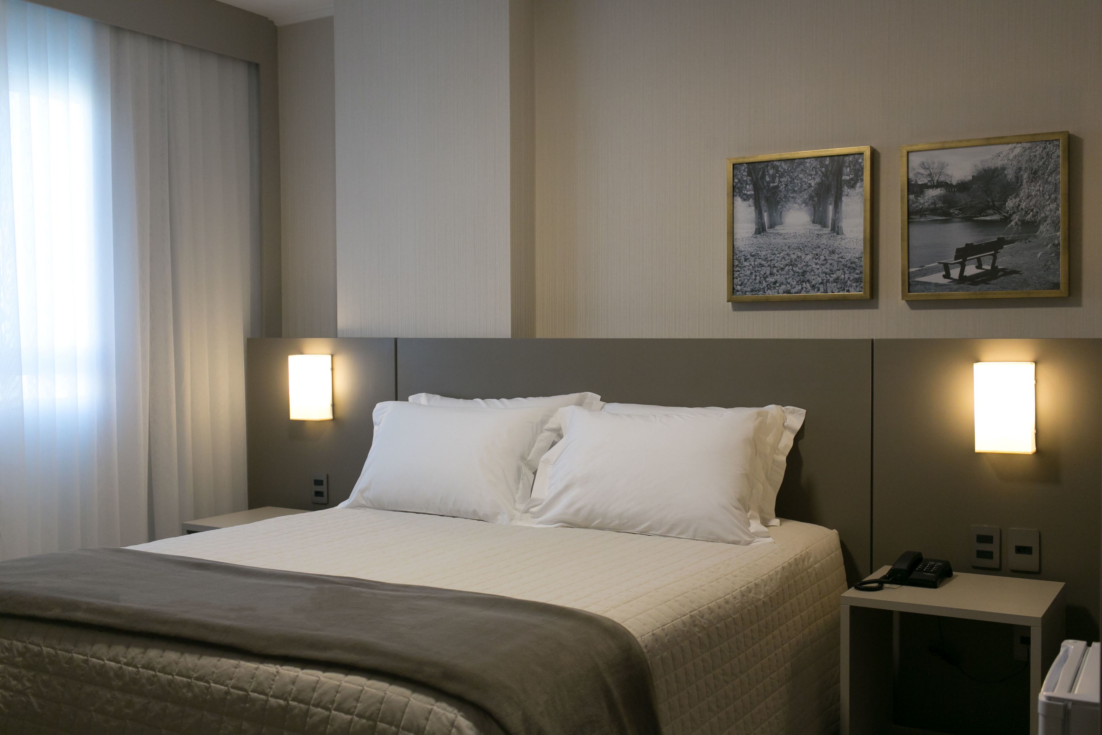 A hotel room with a large bed, two bedside lamps, a nightstand with a phone, and two framed pictures on the wall.