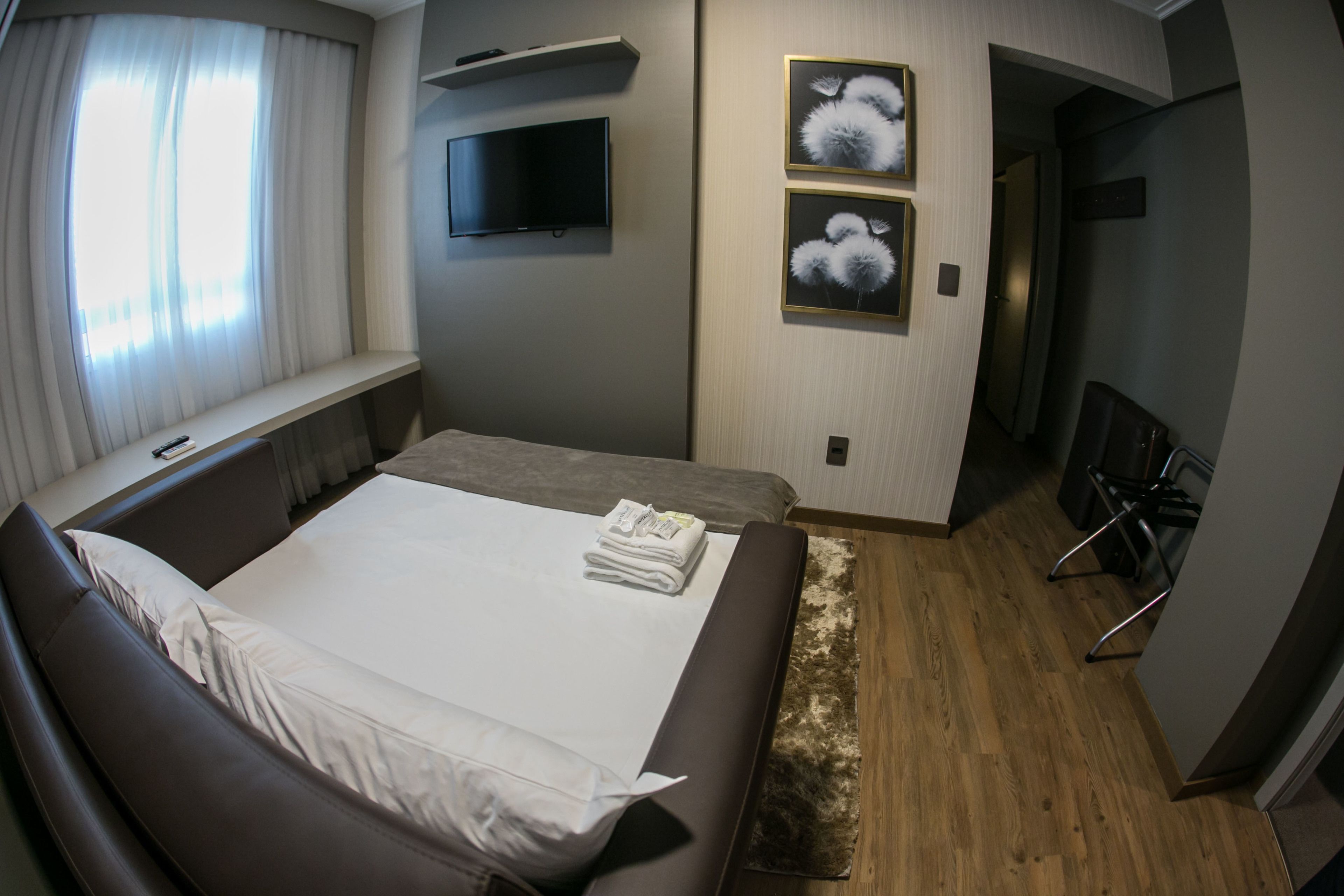 Habitación de hotel moderna con una cama grande, un televisor de pantalla plana en la pared y dos cuadros enmarcados con motivos florales.
