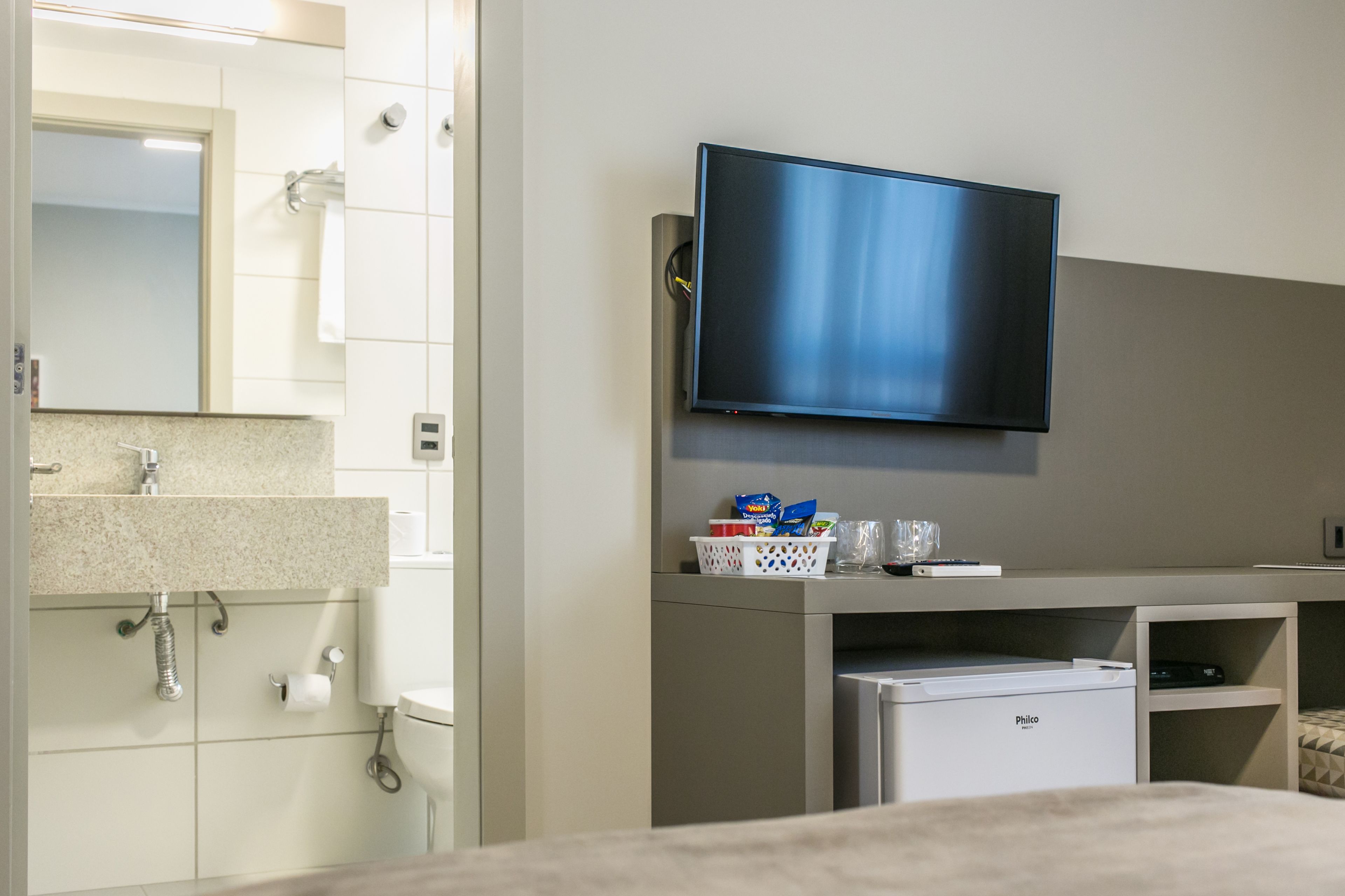 Une chambre d’hôtel moderne équipée d’un téléviseur à écran plat fixé au mur, d’un petit réfrigérateur et d’un lavabo avec un plan de travail.