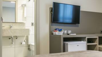 Una habitación de hotel moderna con un televisor de pantalla plana en la pared, un refrigerador pequeño y un lavamanos con encimera.