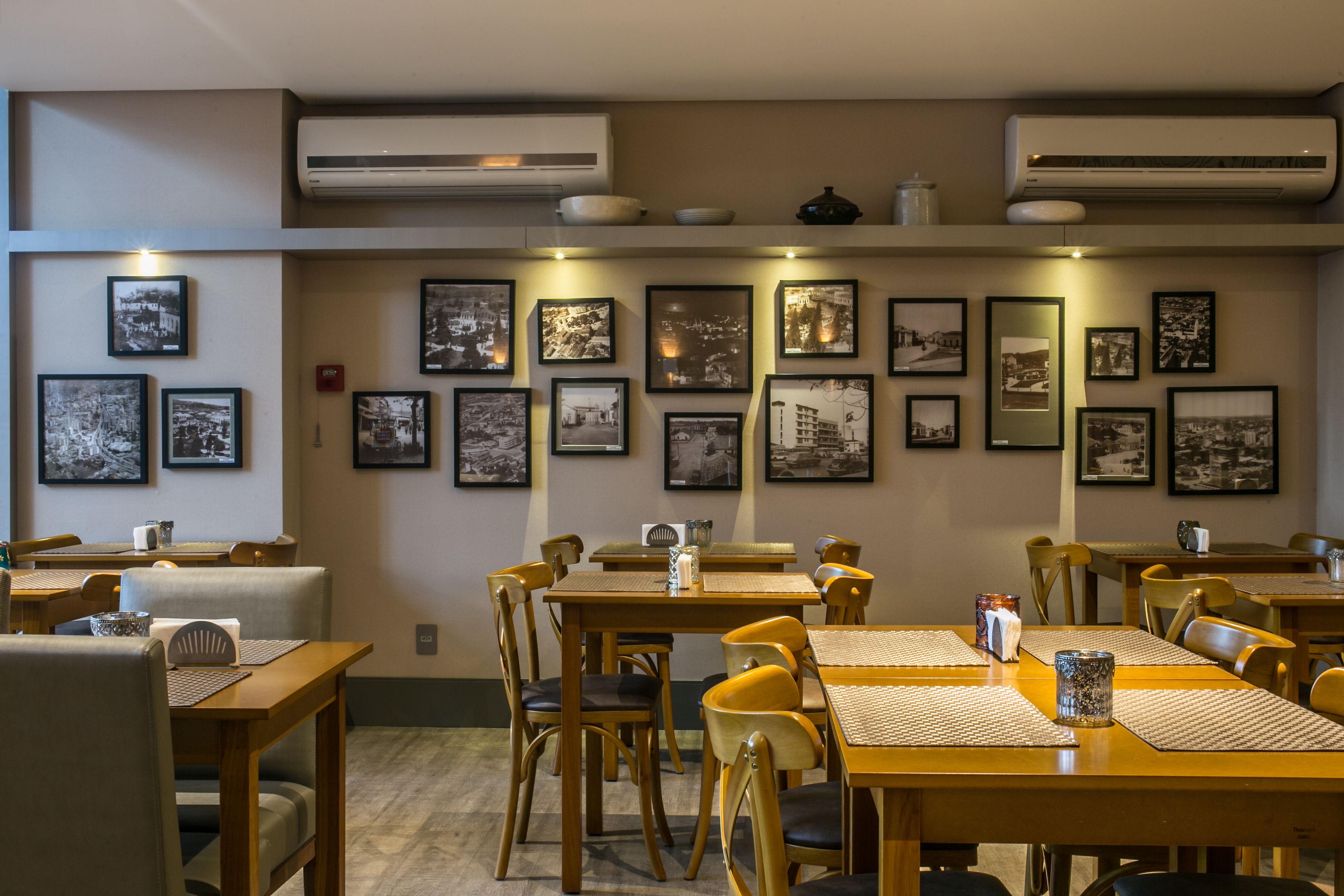 A restaurant with multiple tables and chairs, air conditioning units, and framed pictures on the walls.