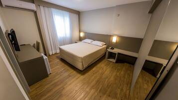 A hotel room with a bed, bedside tables, a desk, and an air conditioning unit.