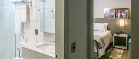 Un baño moderno con inodoro, lavamanos y ducha. Hay una cama con una mesita de noche y un cuadro en la pared.