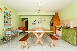 Un comedor con una mesa y bancos de madera, un ventilador de techo y una zona de cocina con un horno de ladrillo.