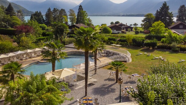 A resort with a pool, outdoor seating, and mountain views. - Hôtel Les Grillons (Talloires-Montmin)