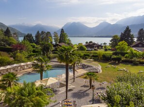A resort with a pool, outdoor seating, and mountain views. - Hôtel Les Grillons (Talloires-Montmin)
