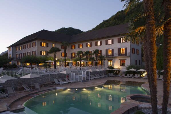 A hotel with a swimming pool, lounge chairs, and umbrellas. - Hôtel Les Grillons (Talloires-Montmin)