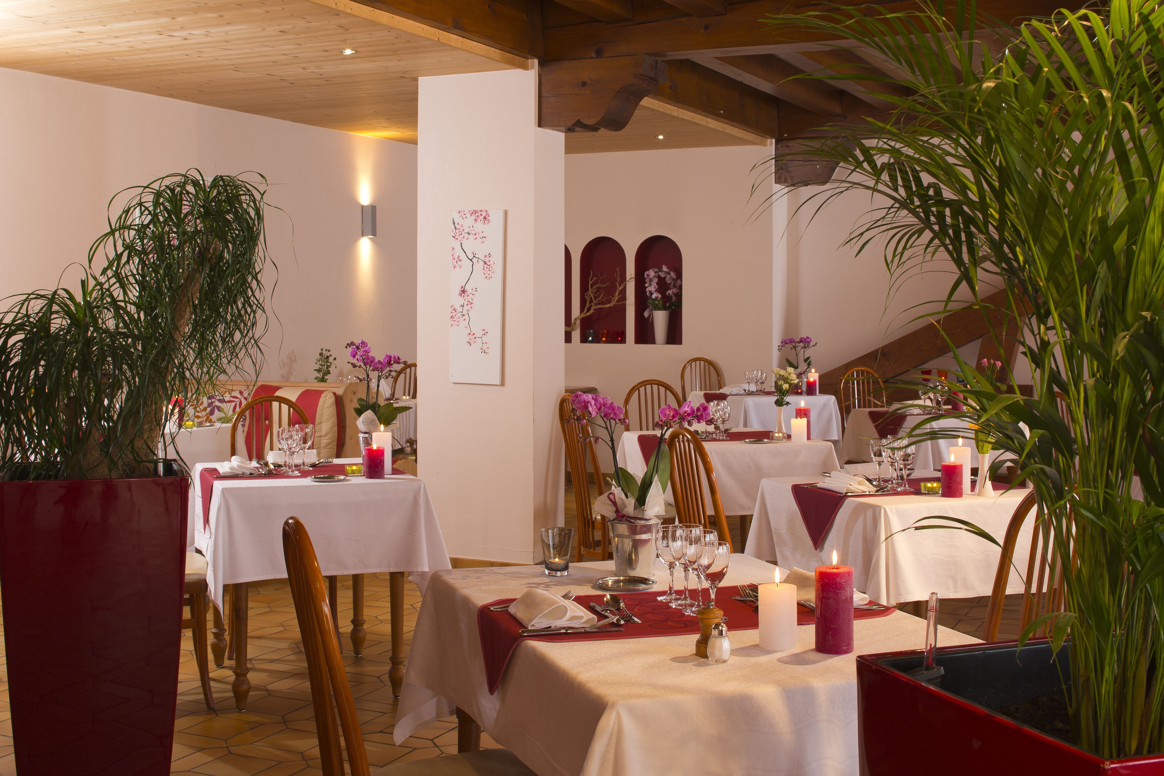 Een restaurant met gedekte tafels, houten stoelen, witte tafellakens en kaarsen.