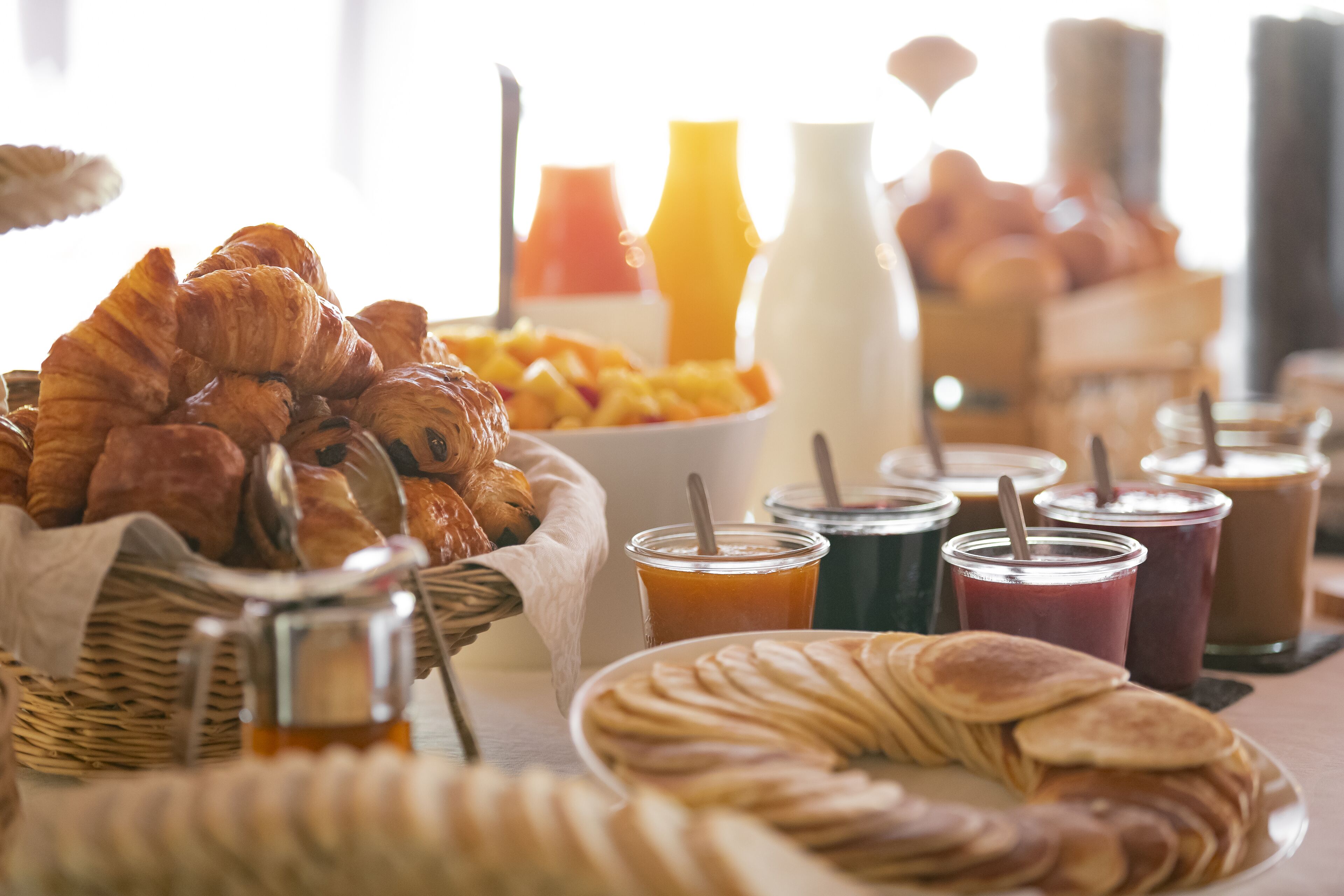 A breakfast buffet with croissants, pancakes, and various beverages.