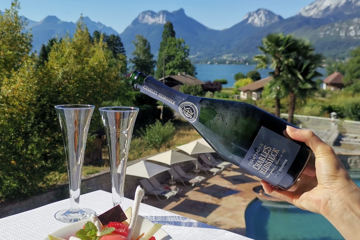 A bottle of Charles Heidsieck champagne being poured into a glass, with a bowl of fruit dessert and two empty glasses on a table.