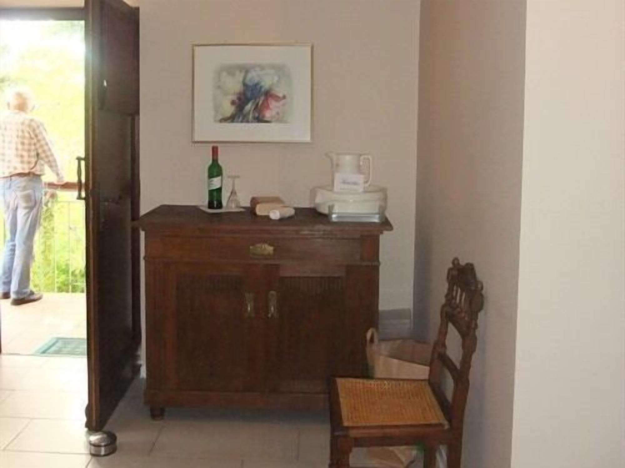 Una habitación con un armario de madera, una silla, un cuadro en la pared y una persona de pie cerca de la puerta.