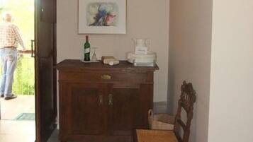 Una habitación con un armario de madera, una silla, un cuadro en la pared y una persona de pie cerca de la puerta.