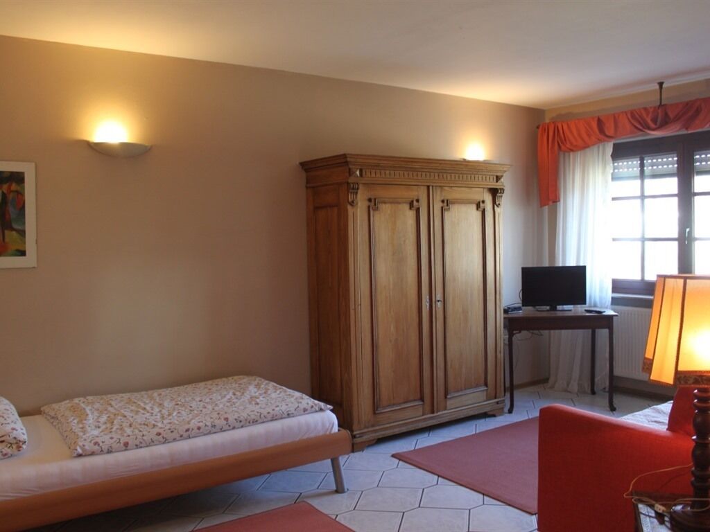 Una habitación con una cama, un armario de madera, un televisor y una ventana con cortinas.