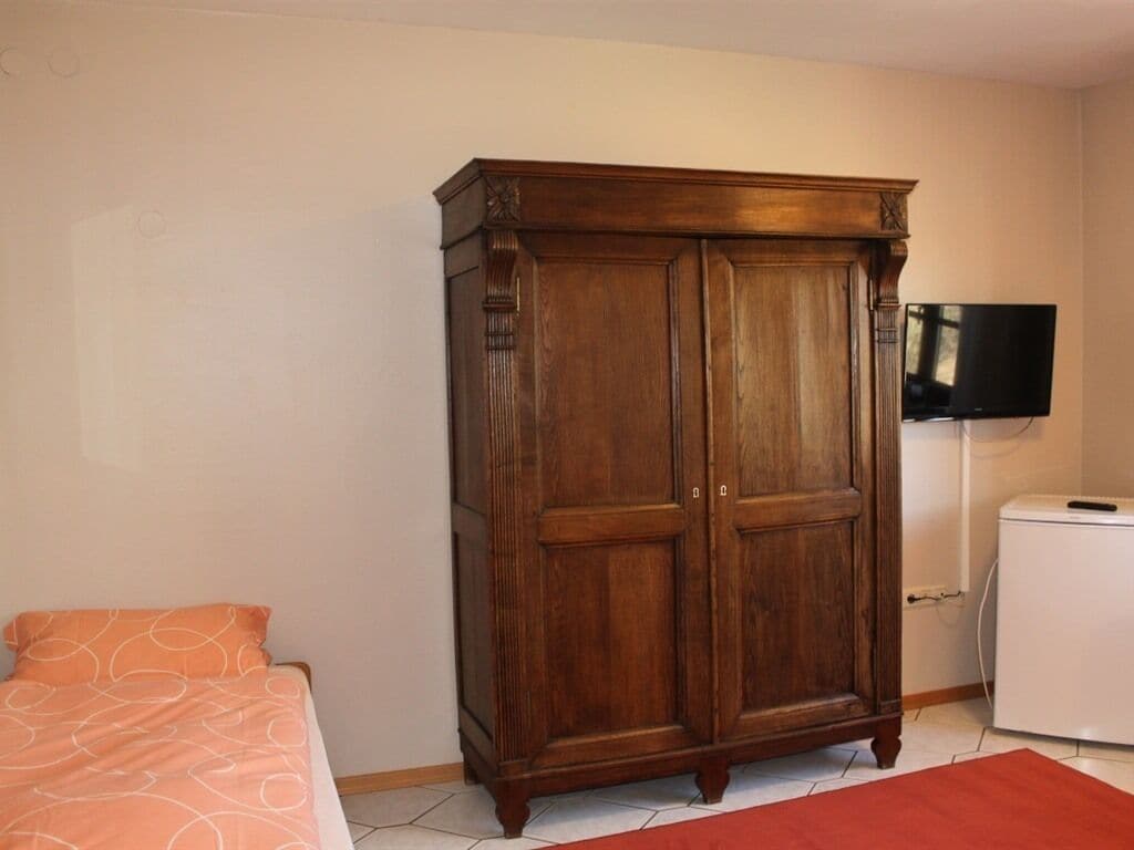 Une chambre avec une armoire en bois, un lit recouvert d’une couvre-lit à motifs orange, un téléviseur et un appareil électroménager blanc.