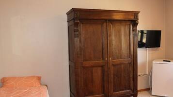 Une chambre avec une armoire en bois, un lit recouvert d’une couvre-lit à motifs orange, un téléviseur et un appareil électroménager blanc.