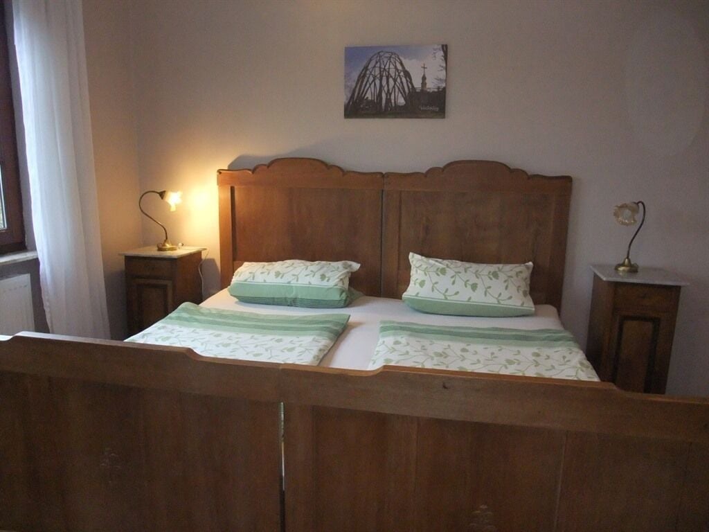 A bedroom with a wooden bed, two bedside tables, a lamp, and a painting on the wall.