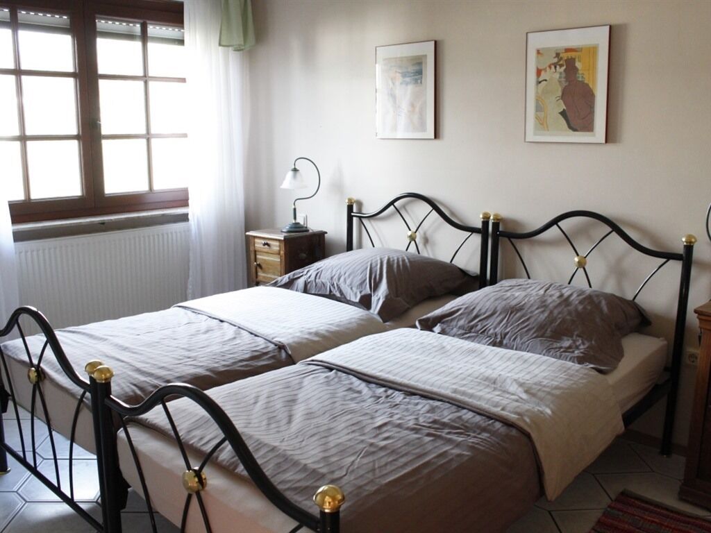 Une chambre avec deux lits, une table de chevet avec une lampe, un radiateur et deux tableaux encadrés au mur.