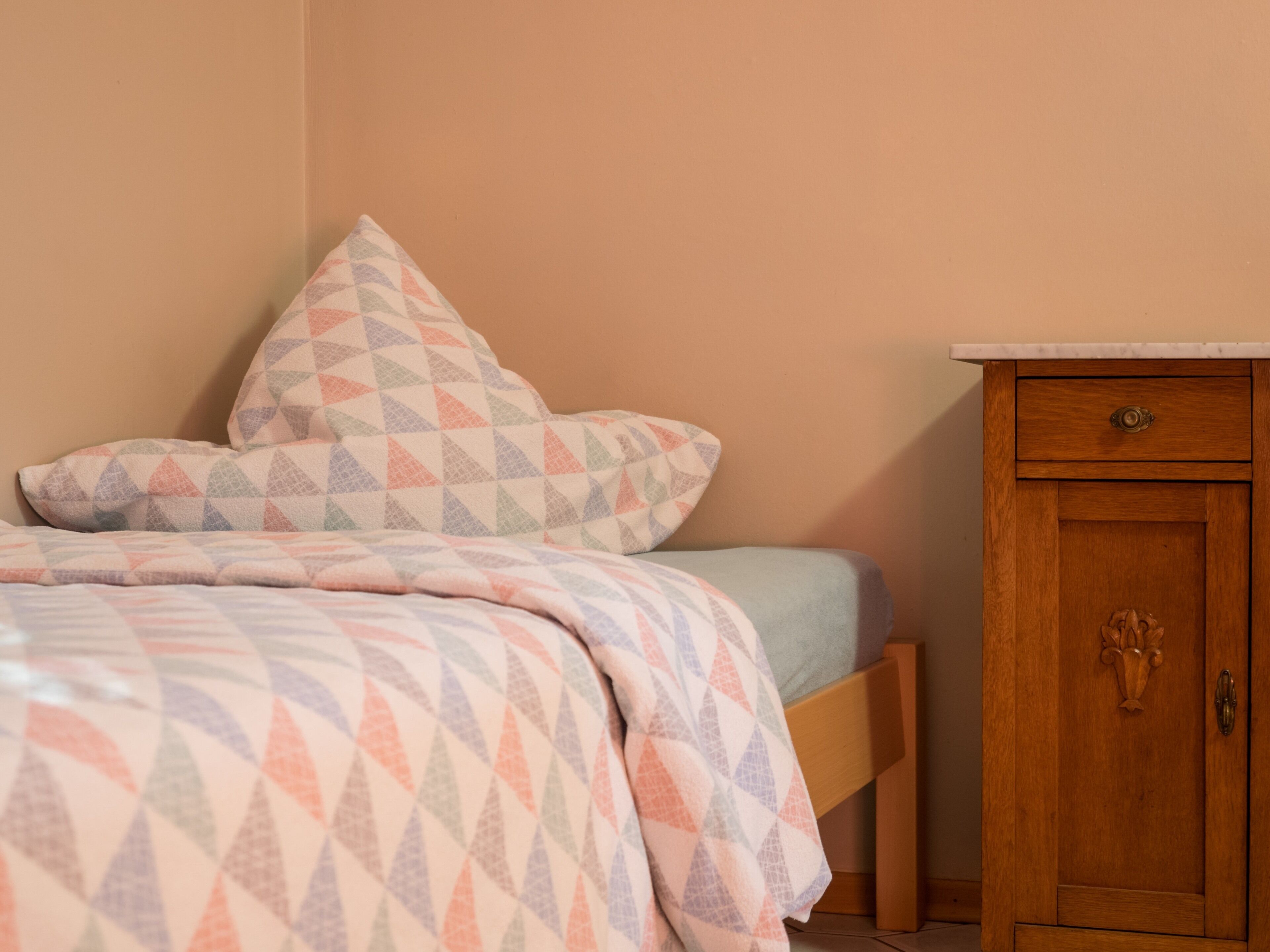 Une chambre à coucher avec un lit, des oreillers, une armoire en bois et une table de chevet.