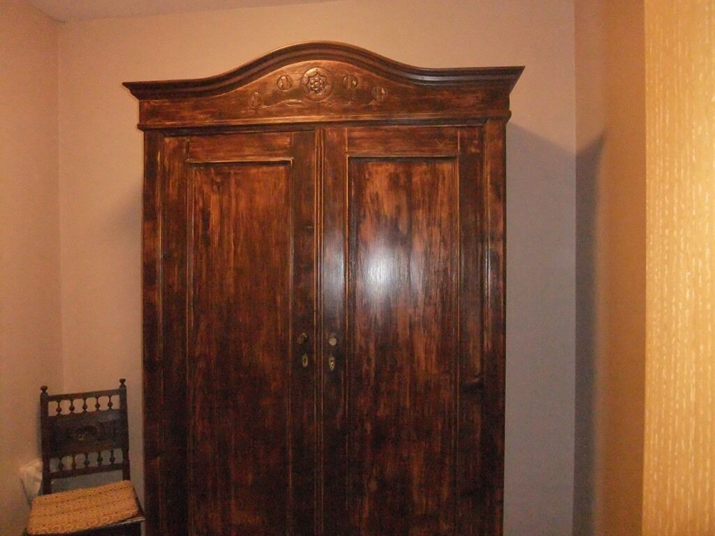 Un armario de madera con dos puertas y un frente curvo, apoyado contra una pared.