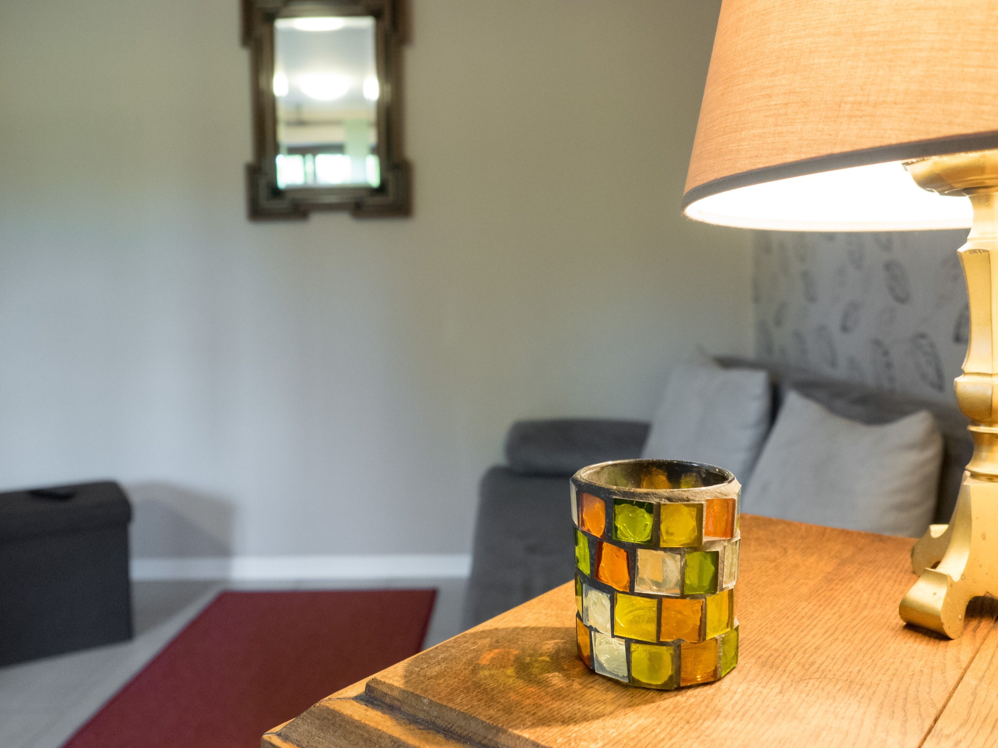 Una mesa de madera con un jarrón de mosaico colorido y una lámpara.
