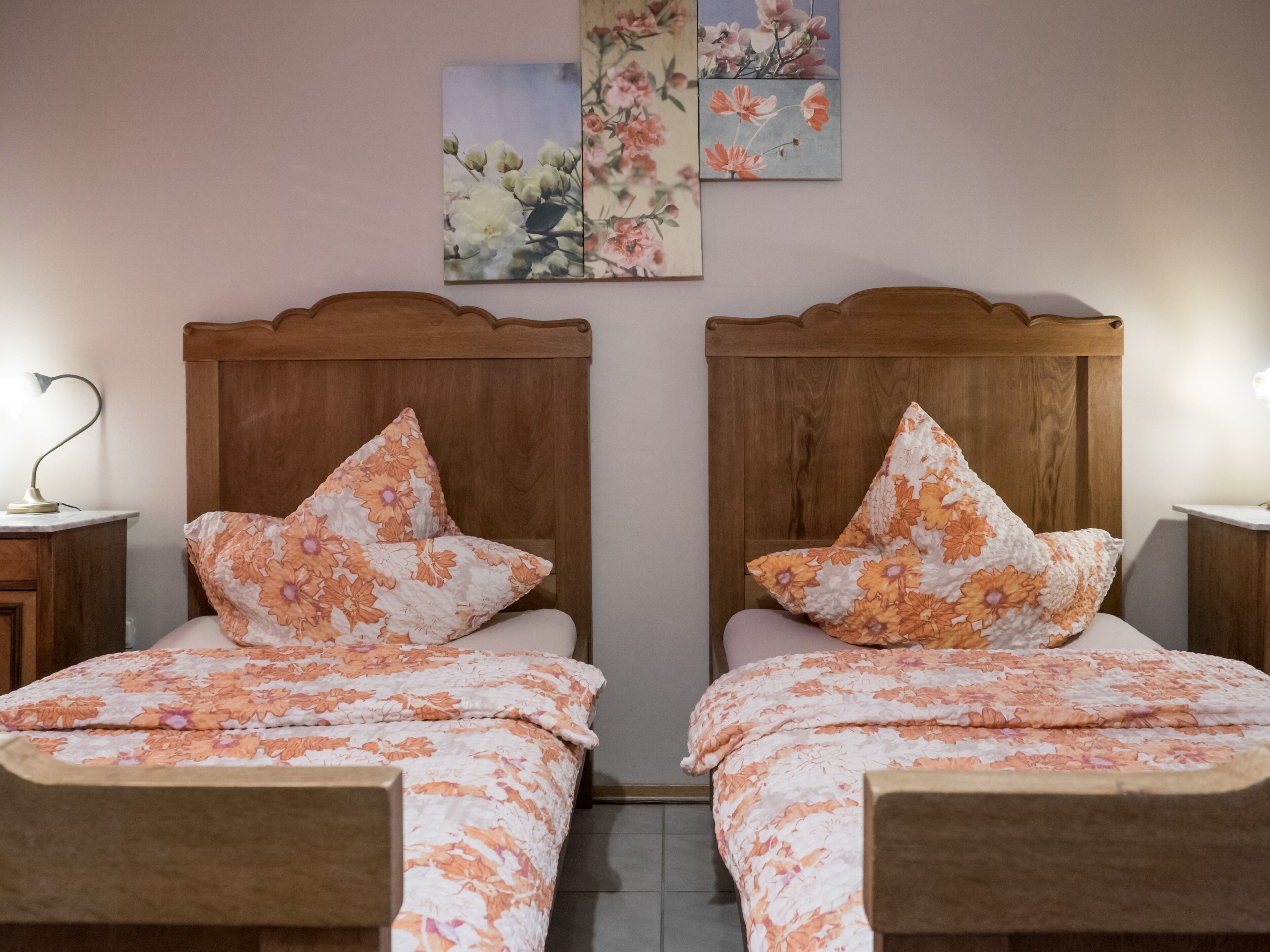 Un dormitorio doble con ropa de cama floral, cabeceros de madera y mesitas de noche con lámparas.