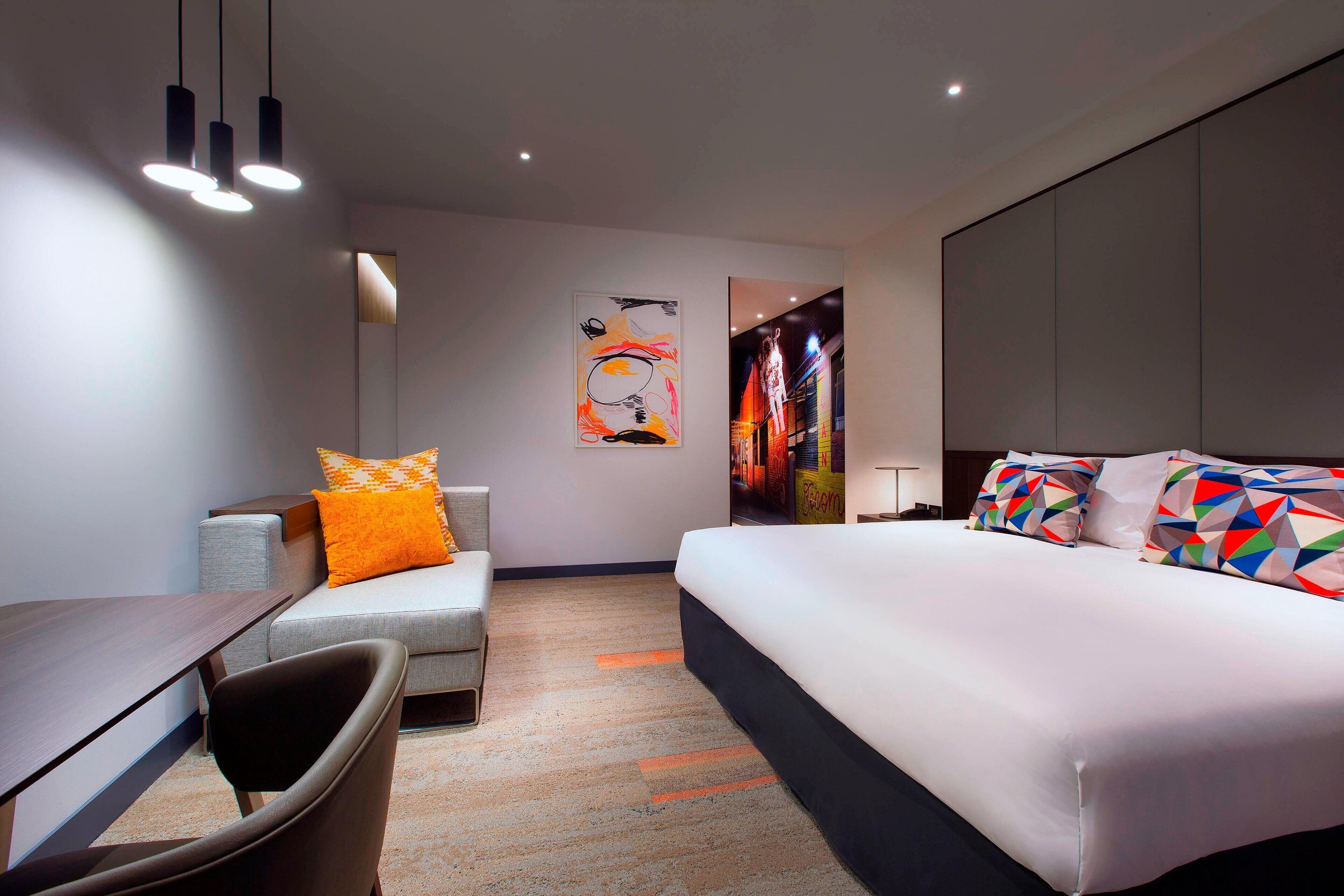 Una habitación de hotel moderna con cama, escritorio, silla y sofá.