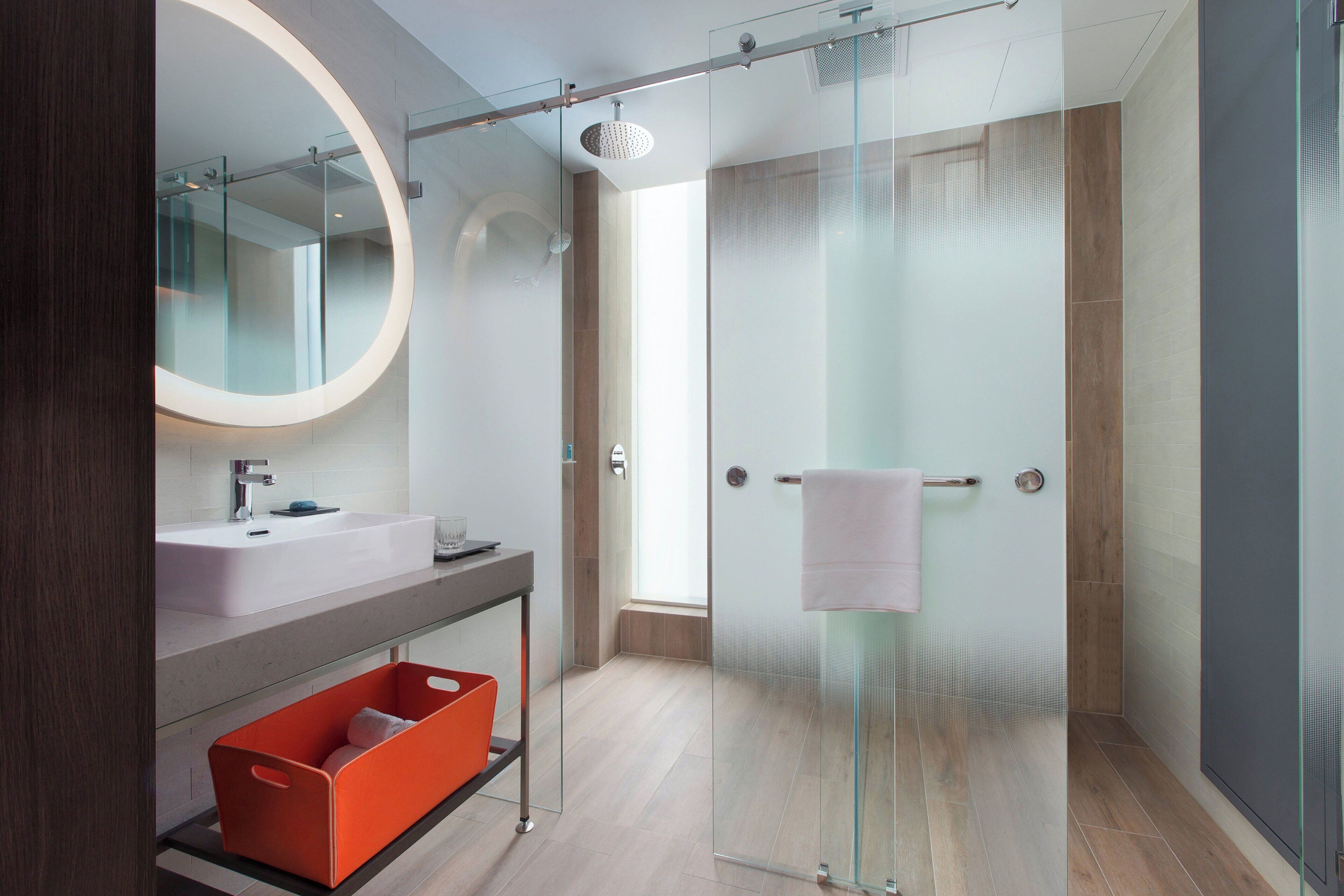 A modern bathroom with a glass-enclosed shower, a large mirror, and a wooden floor.