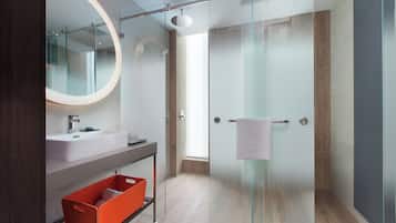 A modern bathroom with a glass-enclosed shower, a large mirror, and a wooden floor.