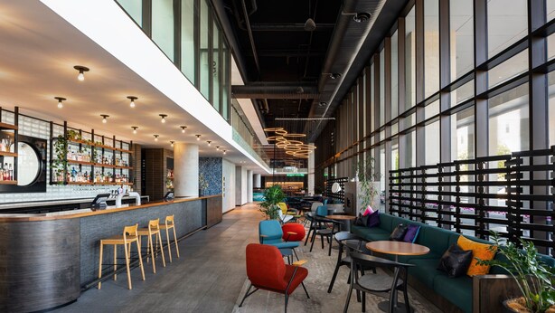 A modern indoor space with a bar area, seating, and large windows. - Aloft by Marriott Perth (Rivervale)