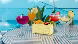A table with four colorful drinks and a small yellow ice cream bar, set against a poolside view. - Aloft by Marriott Perth (Rivervale)