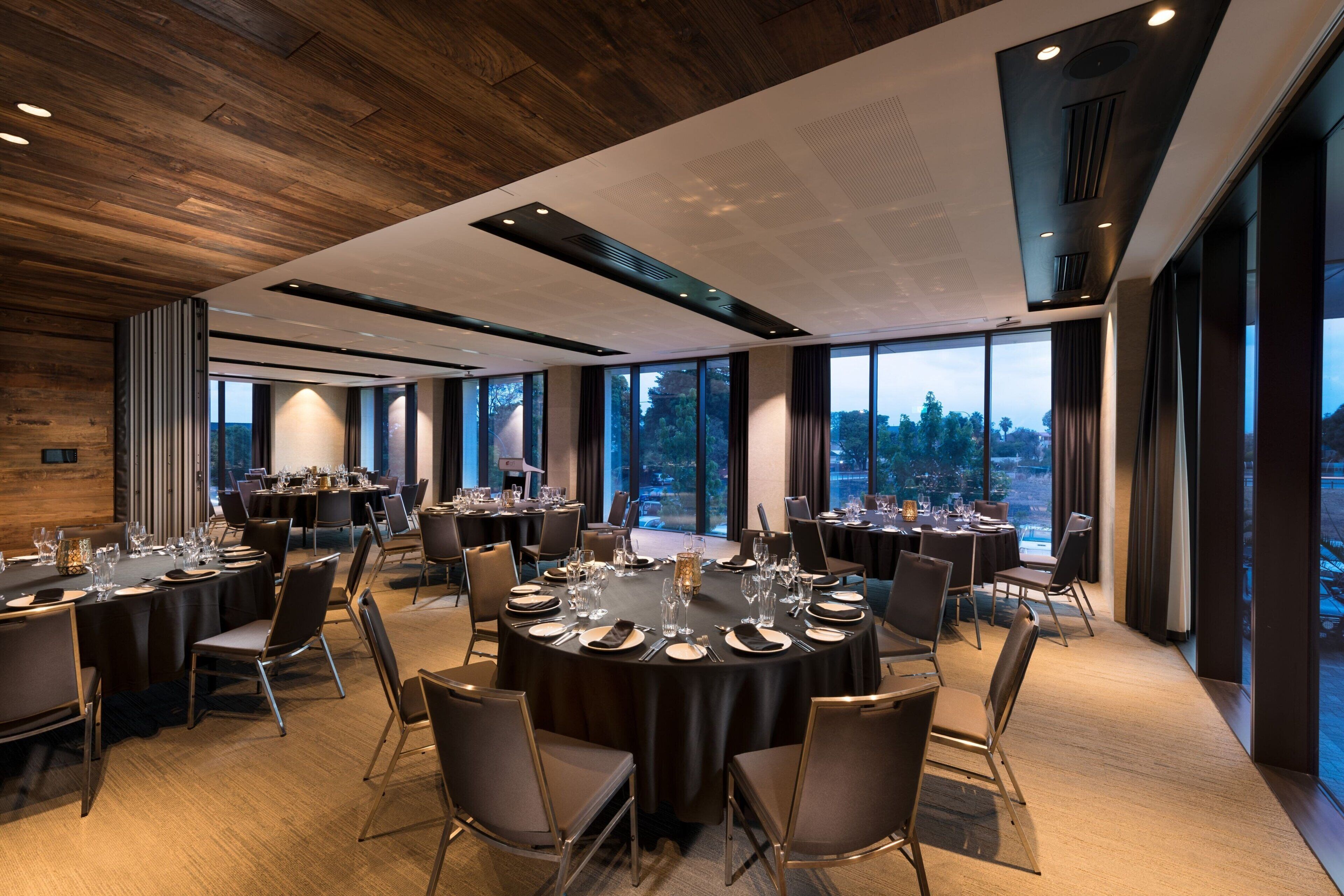 A modern dining area with round tables, chairs, and large windows offering a view of the outdoors.