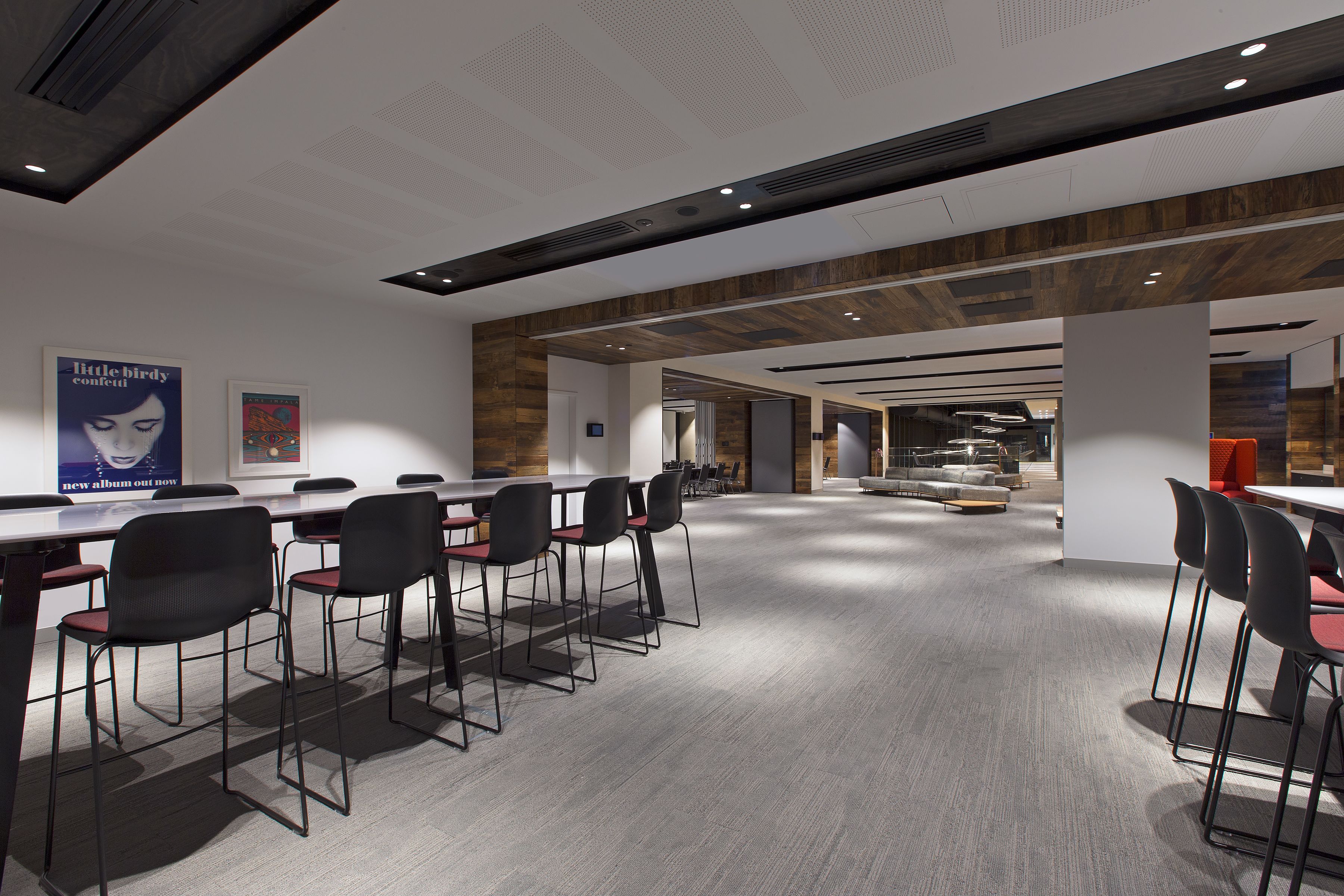 A modern conference room with a long table and multiple chairs, wooden accents on the ceiling, and a poster on the wall.