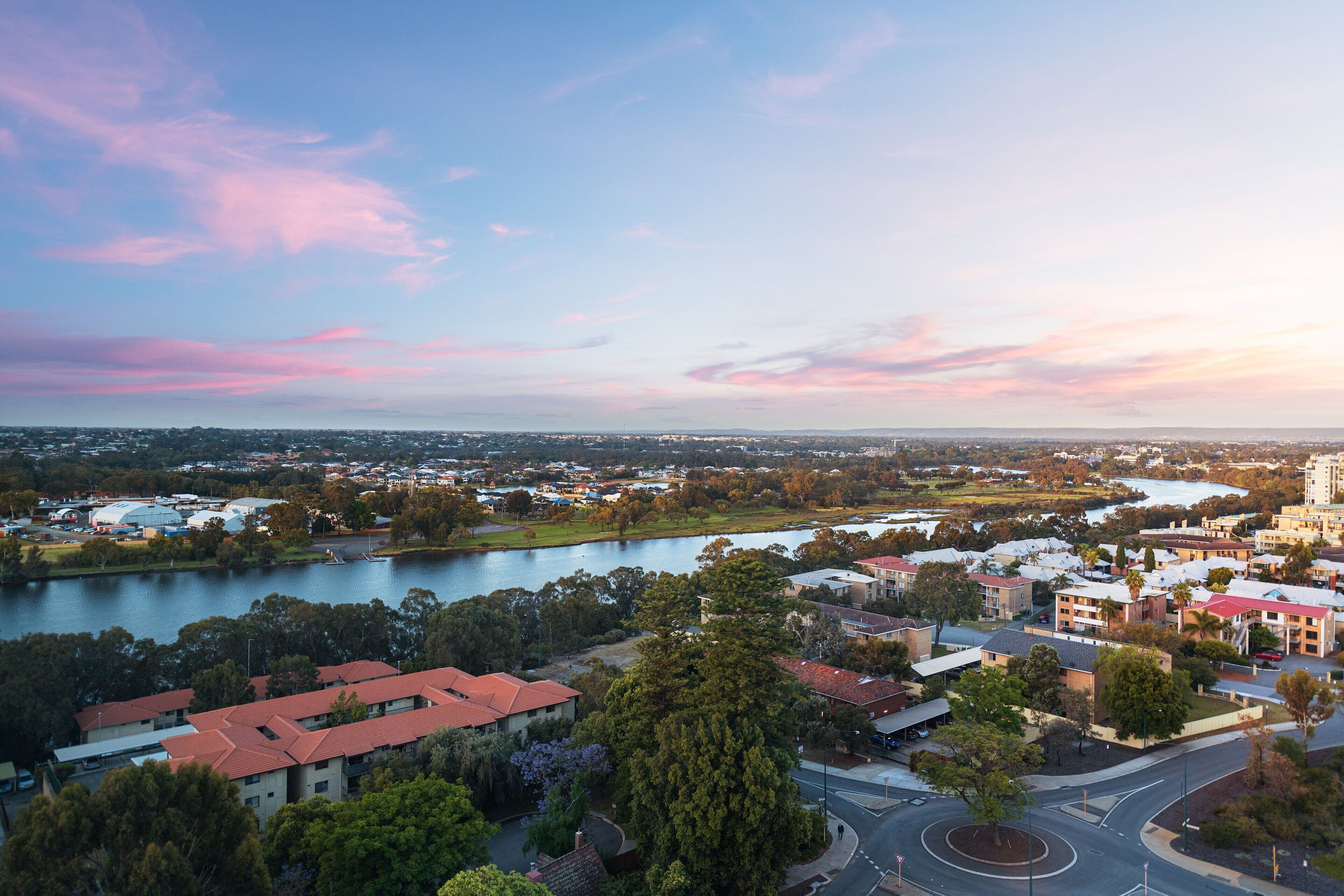 A panoramic view of a town with a river, buildings, and a park.