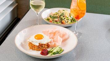 A table with a plate of food, a glass of white wine, and a cocktail with an orange slice.