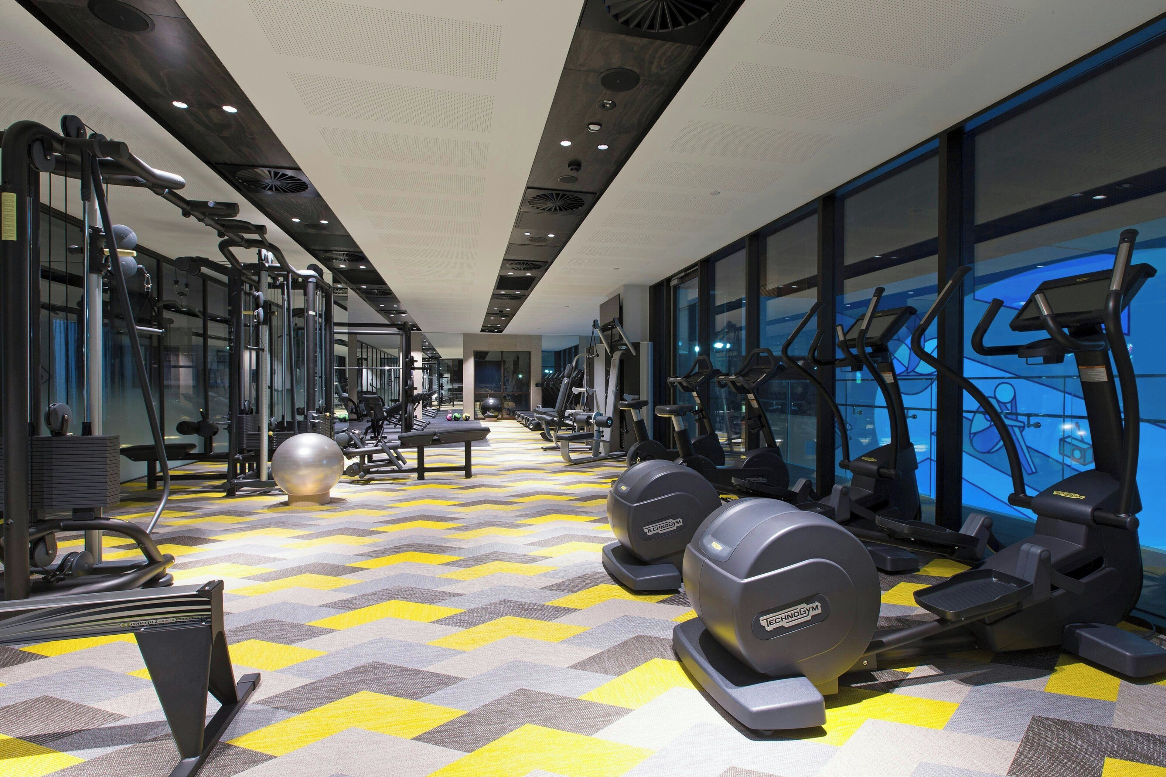 Un gimnasio con equipamiento de ejercicio, paredes con espejos y suelo estampado.