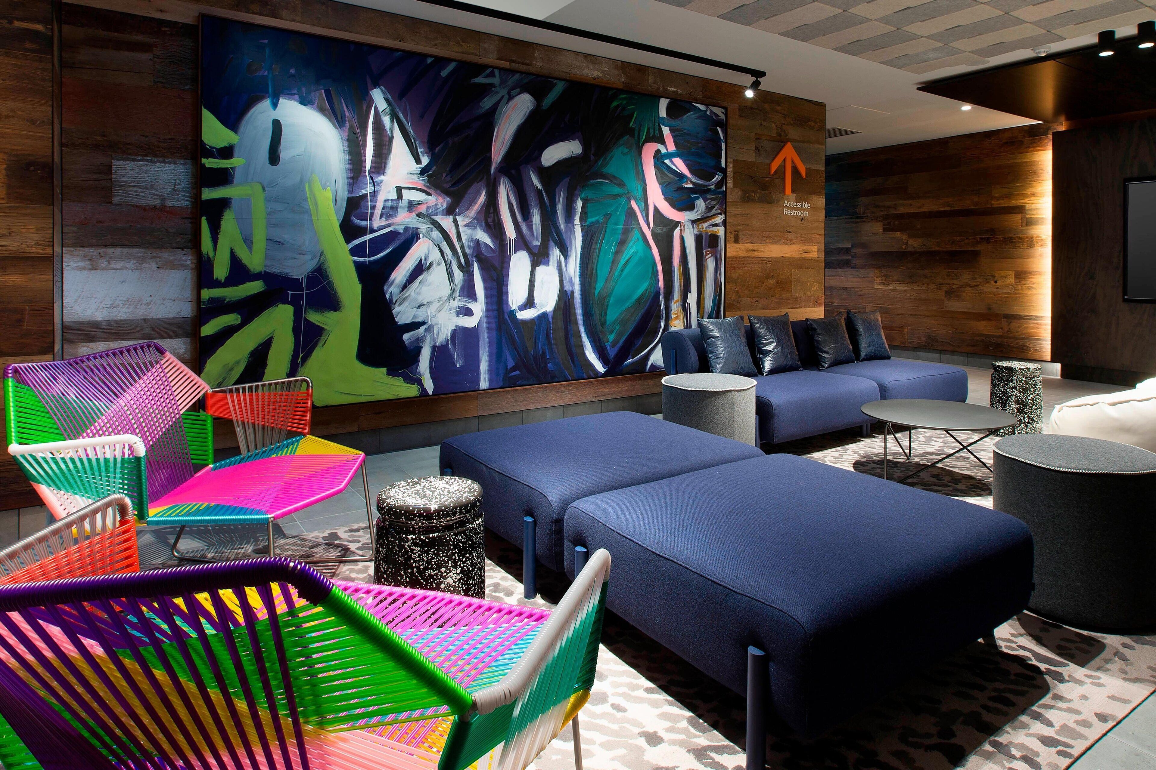 A modern lounge area with colorful chairs, a large abstract painting, and a blue sofa set.