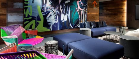 A modern lounge area with colorful chairs, a large abstract painting, and a blue sofa set.