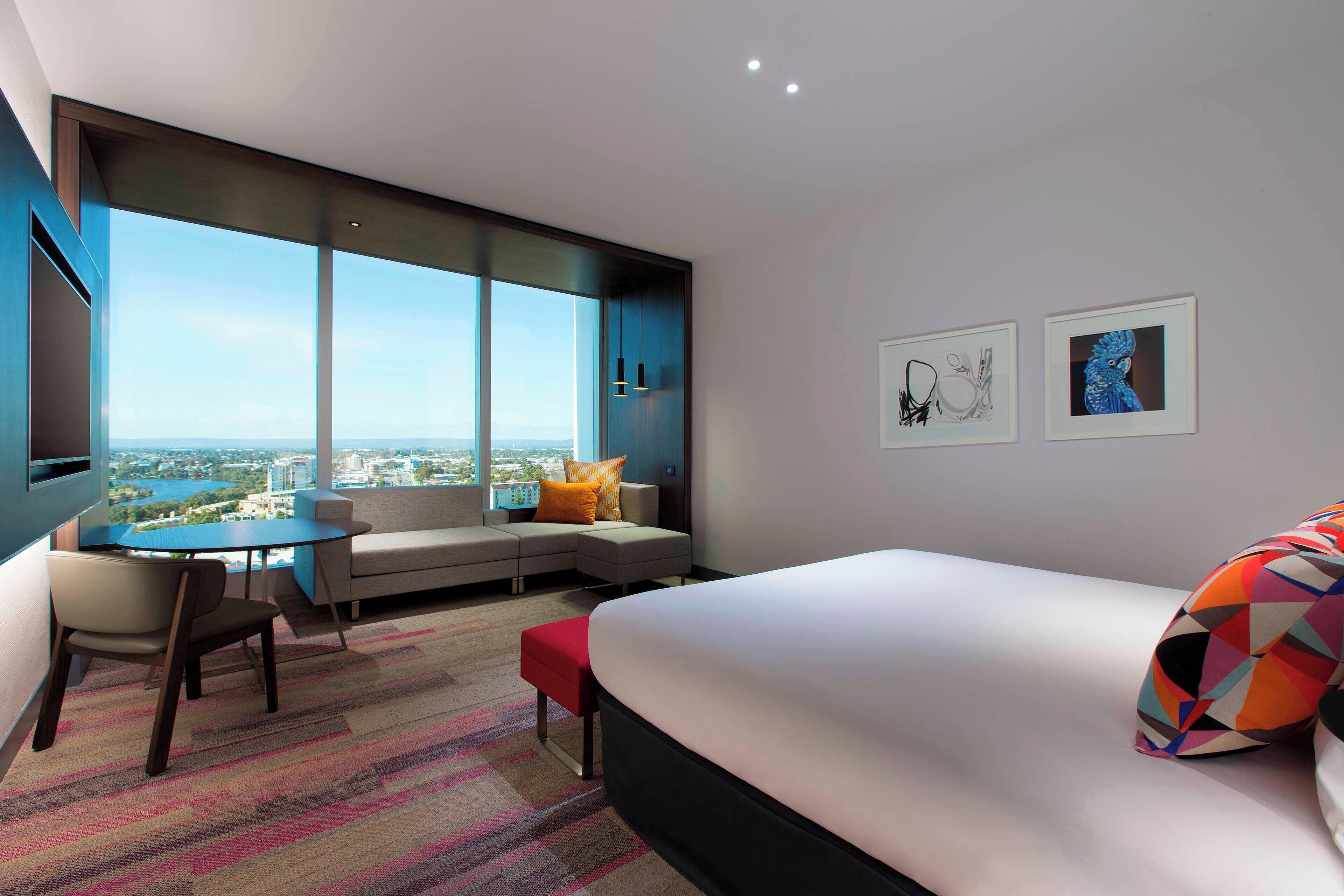 A modern hotel room with a large bed, a seating area with a view, a desk, and artwork on the walls.