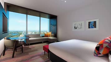 A modern hotel room with a large bed, a seating area with a view, a desk, and artwork on the walls.