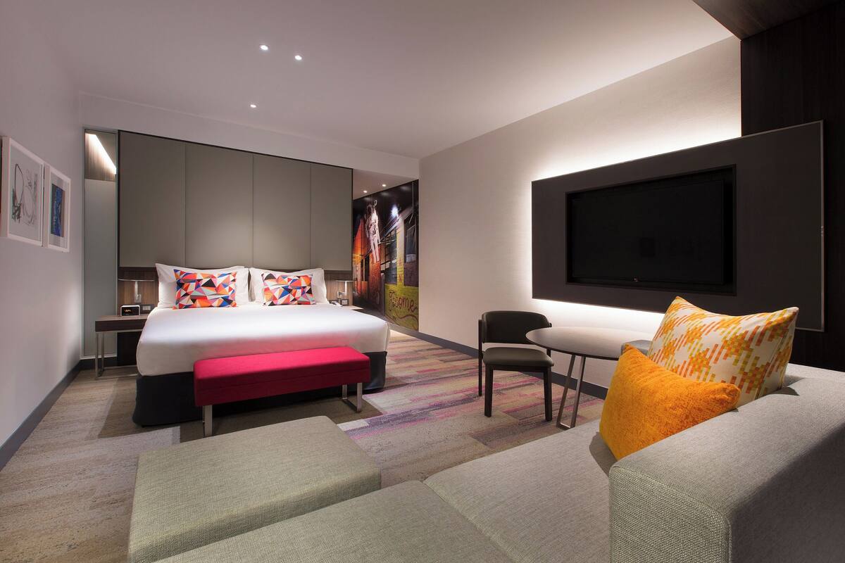 Et moderne hotelværelse med en stor seng, en sofa, et fjernsyn og et skrivebord.