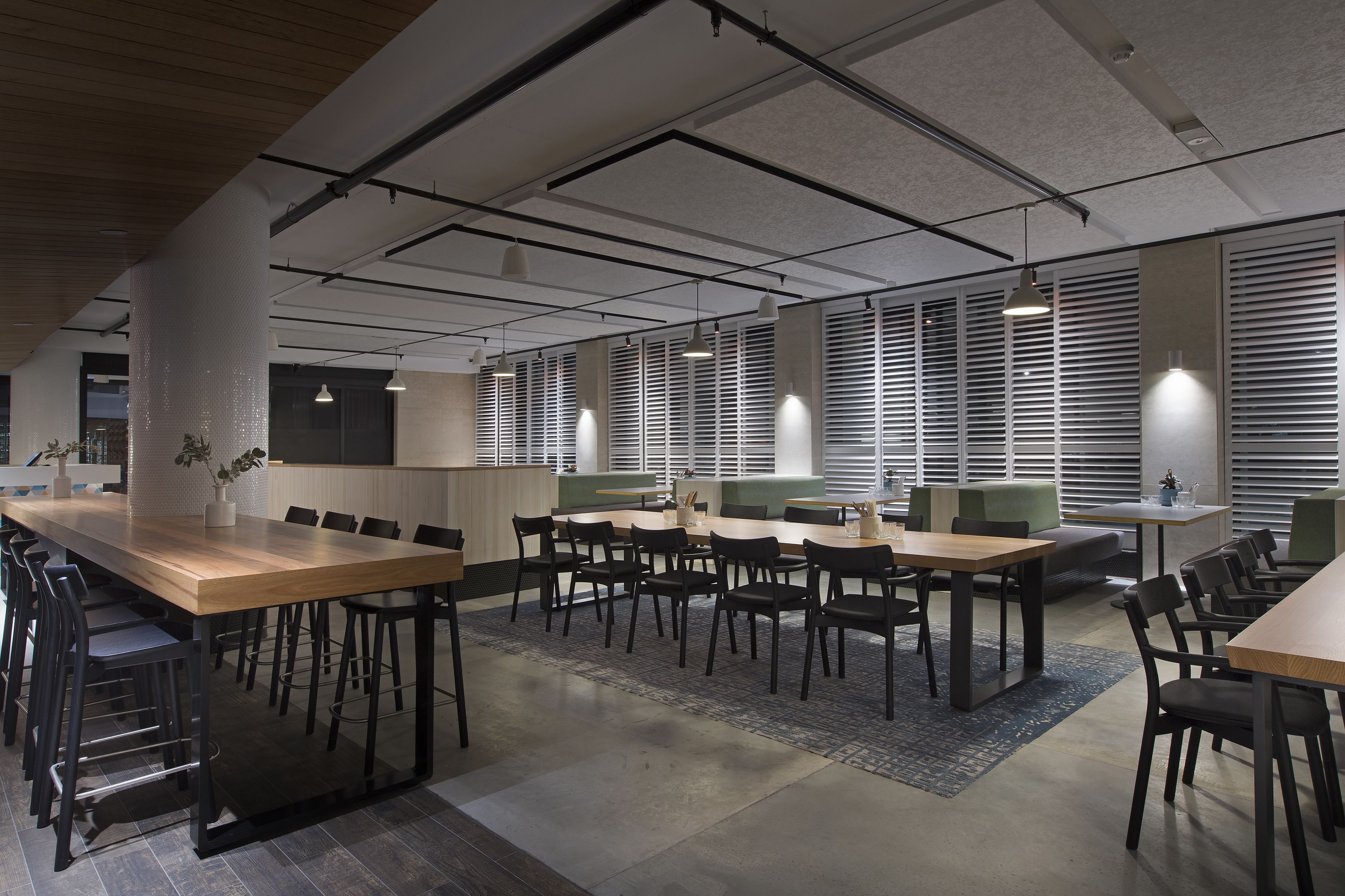 A spacious conference room with multiple tables and chairs, large windows with blinds, and pendant lighting.