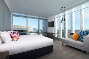 A modern hotel room with a large bed, a sofa, a desk, and a TV.