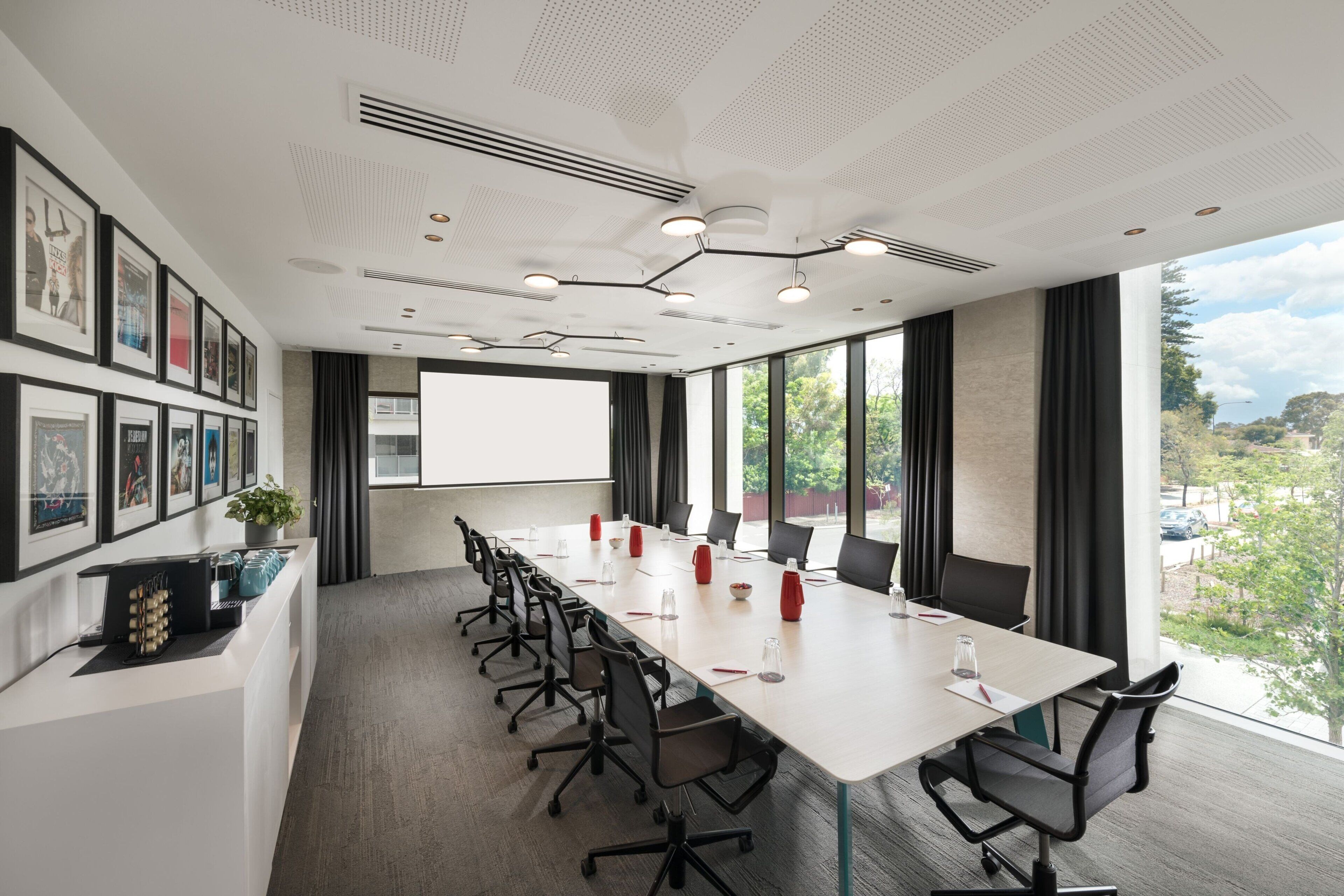 A conference room with a long table, chairs, a projector screen, and framed pictures on the wall.