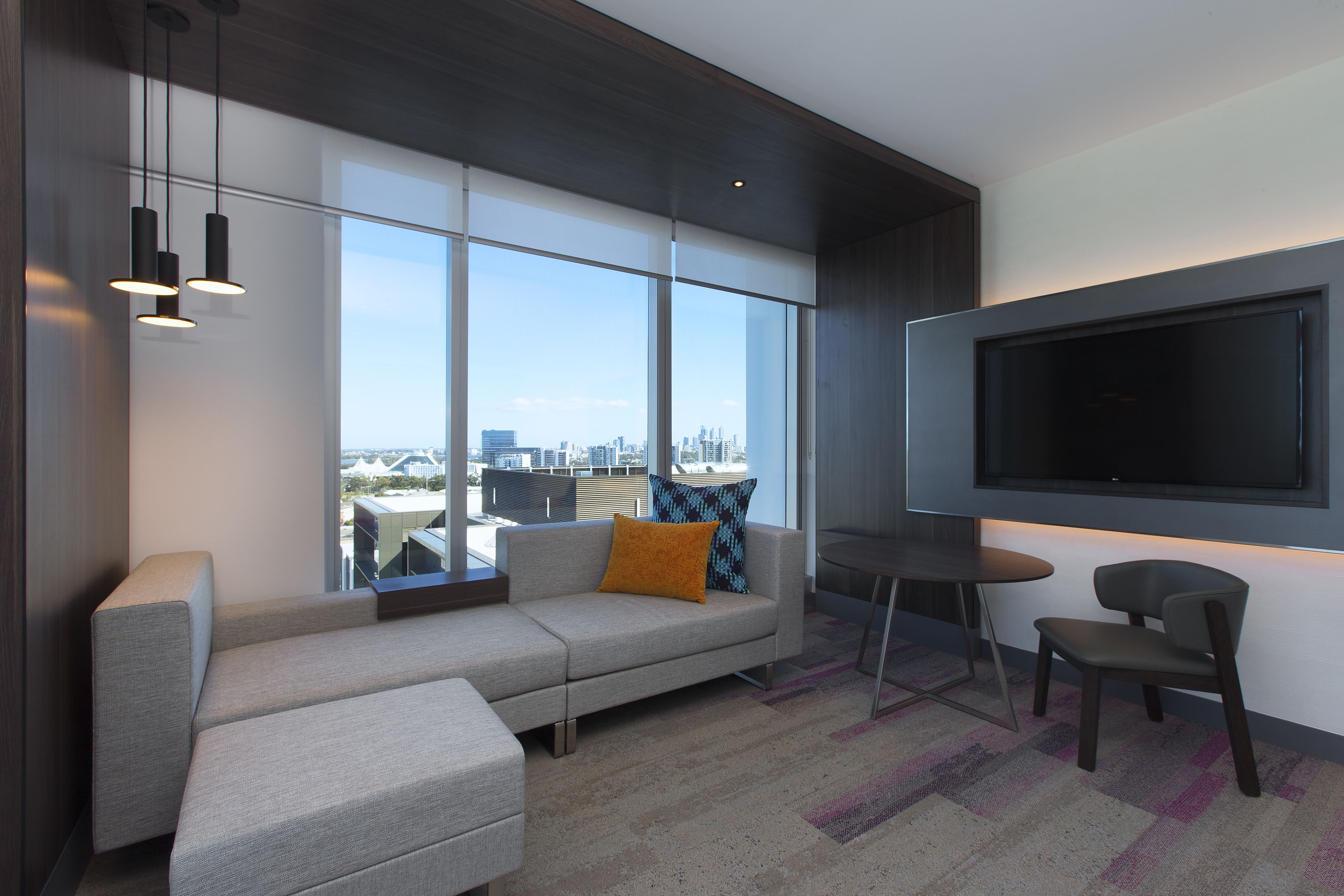 A modern living room with a large TV, a sofa, a coffee table, and a view of the city.